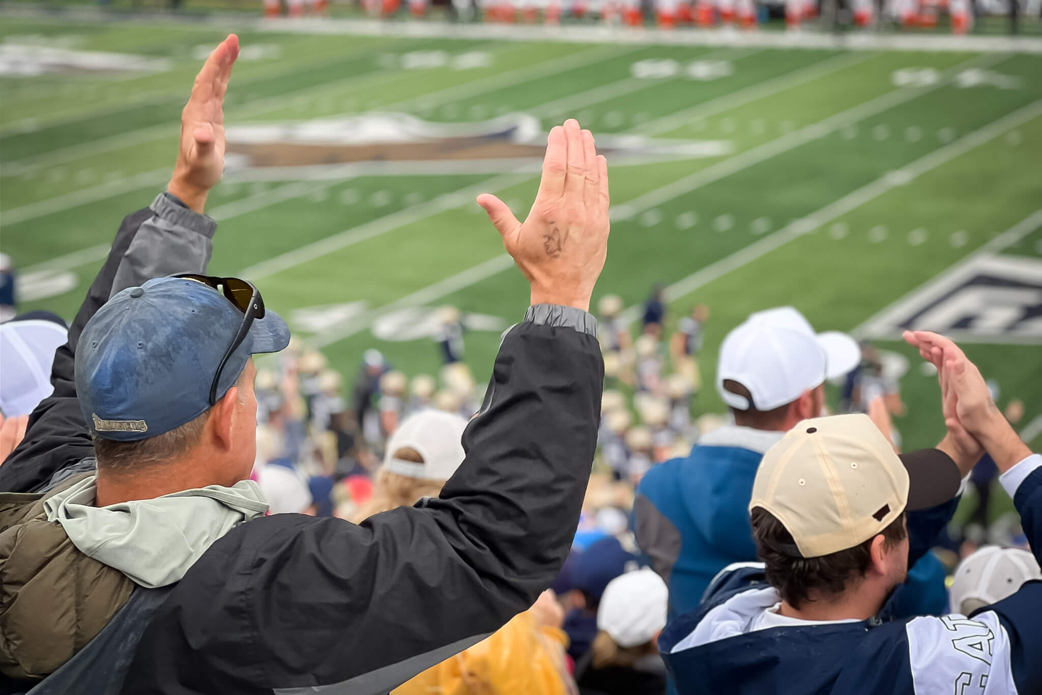 Image of a middle aged white man in the stands, taken from the back, as he celebrates a Montana State University touchdown.