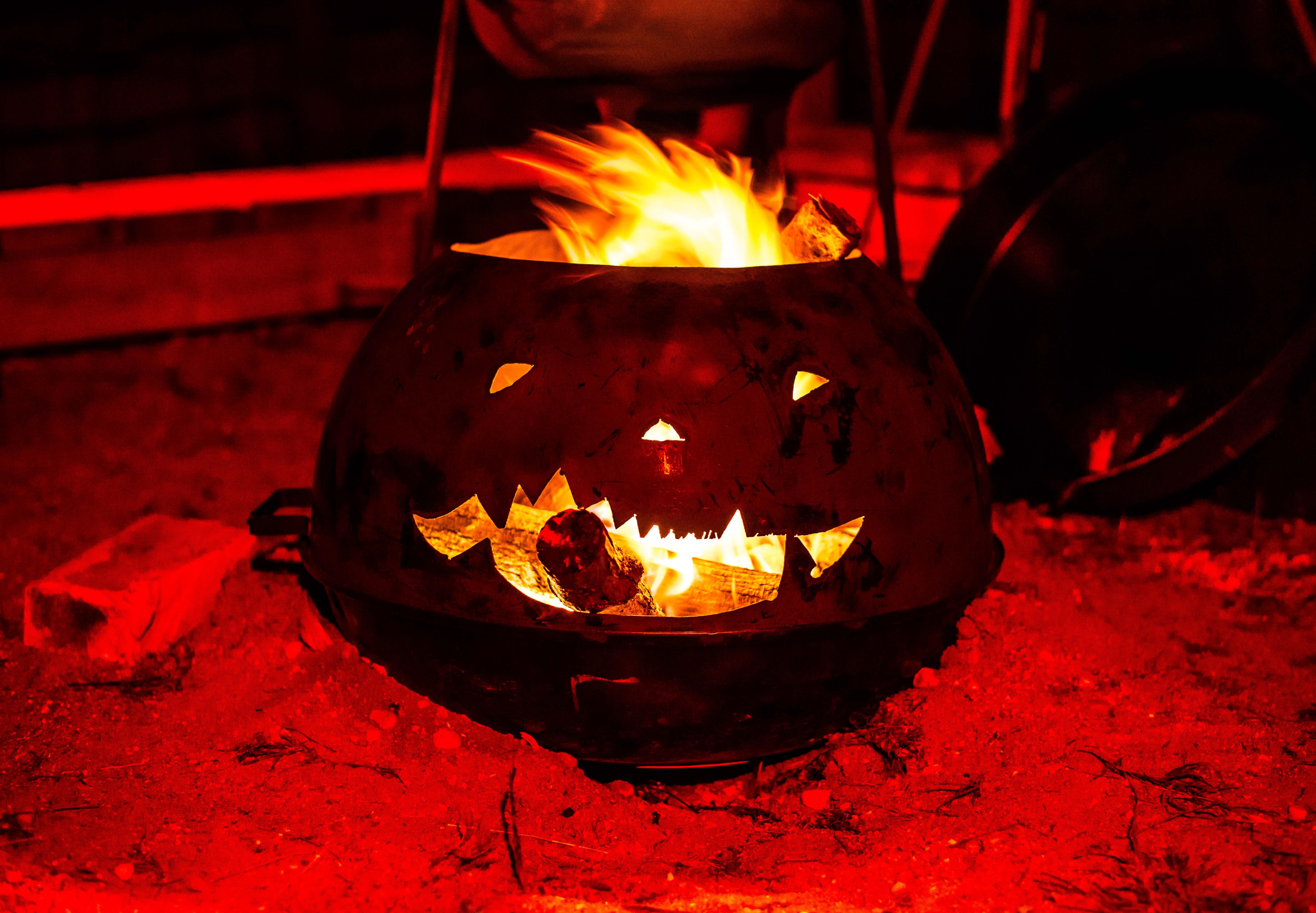 Image of a metal outdoor fireplace cut like a happy jack-o-lantern with a log coming out of its mouth that looks like a cigar.