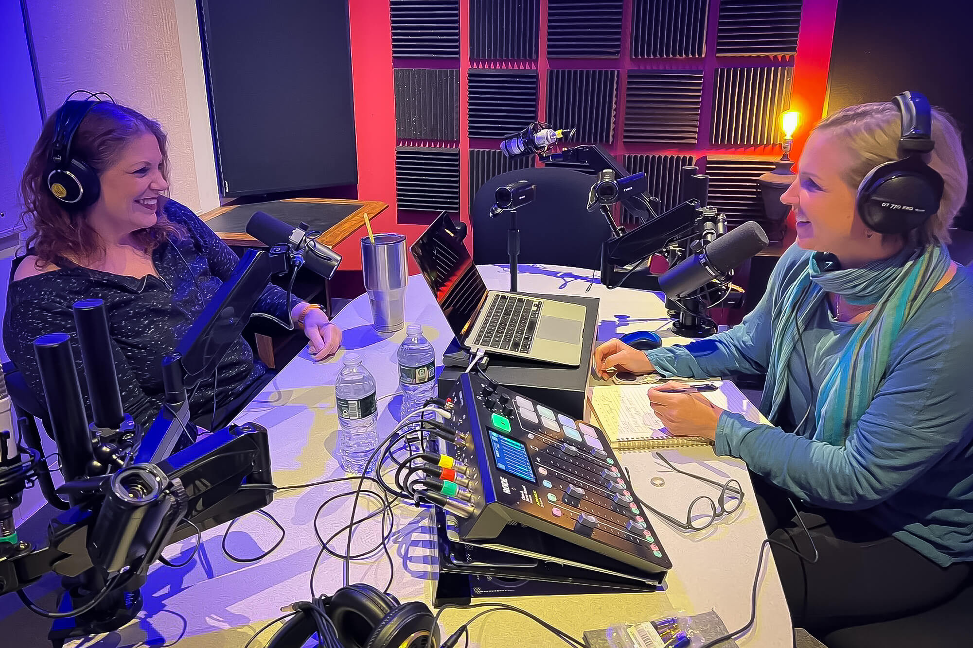Two white women in a podcast studio facing one another while recording a conversation.