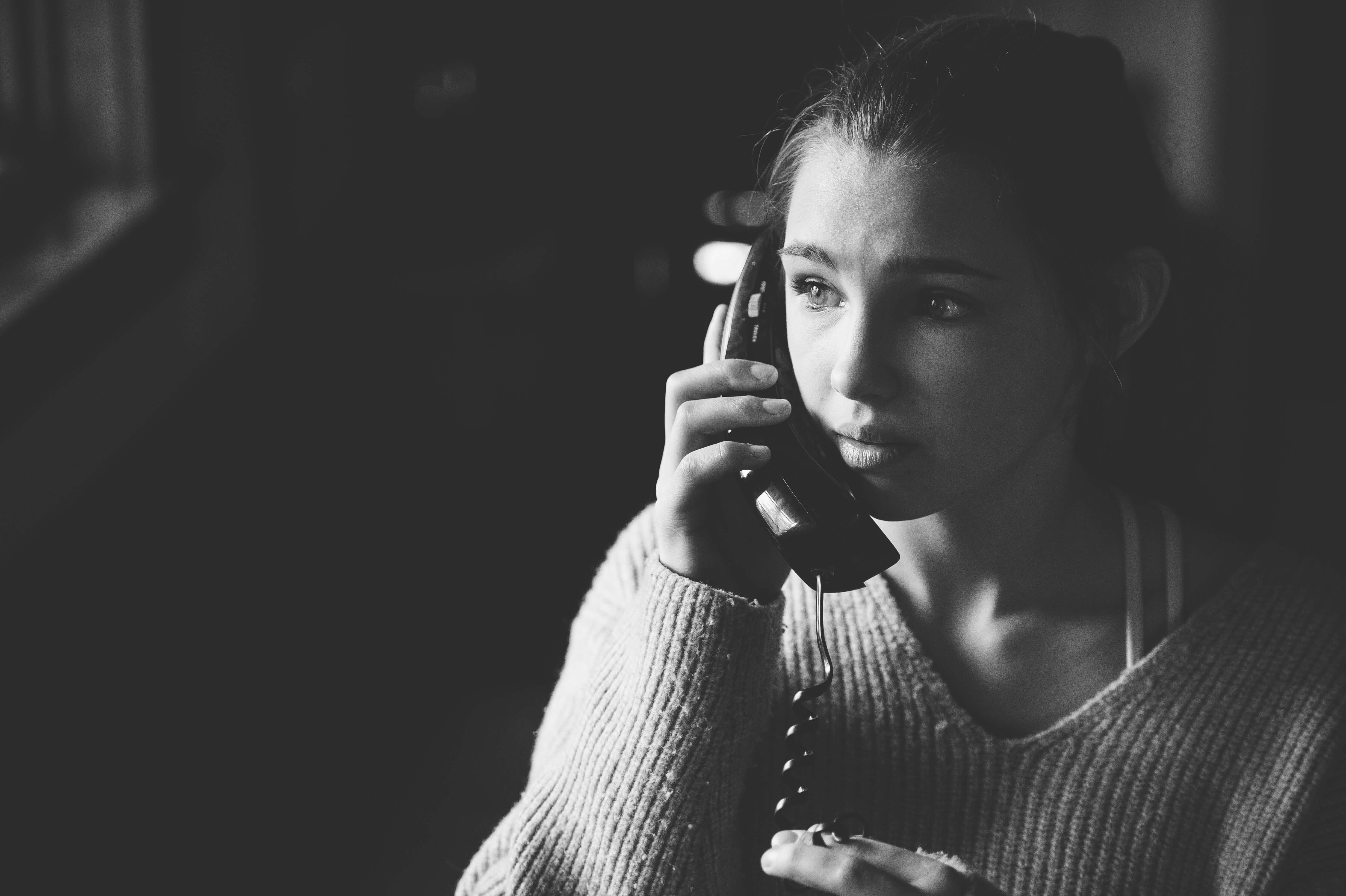 Black and white photo of a white 13 year old girl with an old school telephone against her ear.