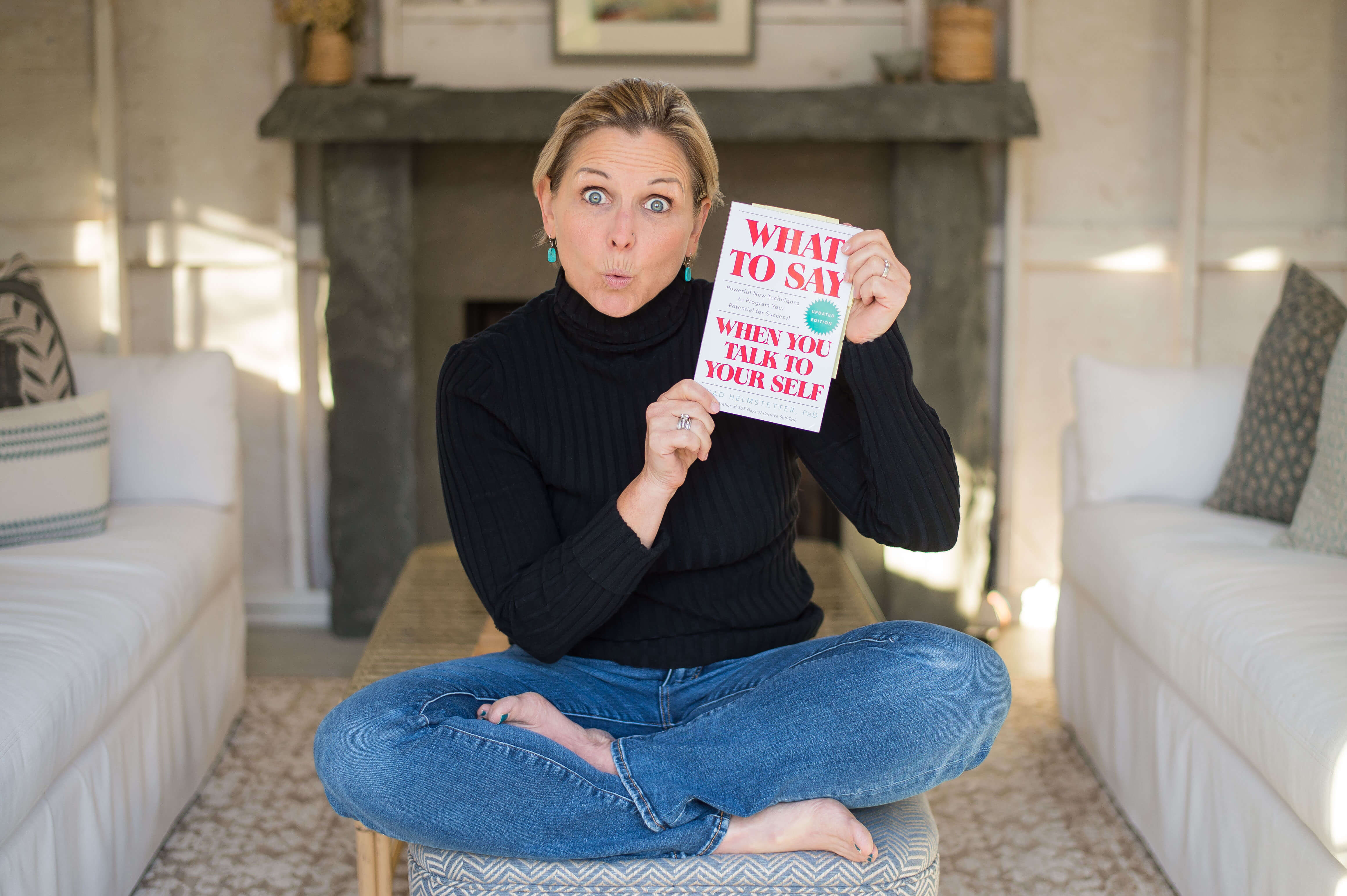 Image of a middle aged white woman holding the book What To Say When You Talk to Yourself with a surprised look on her face.