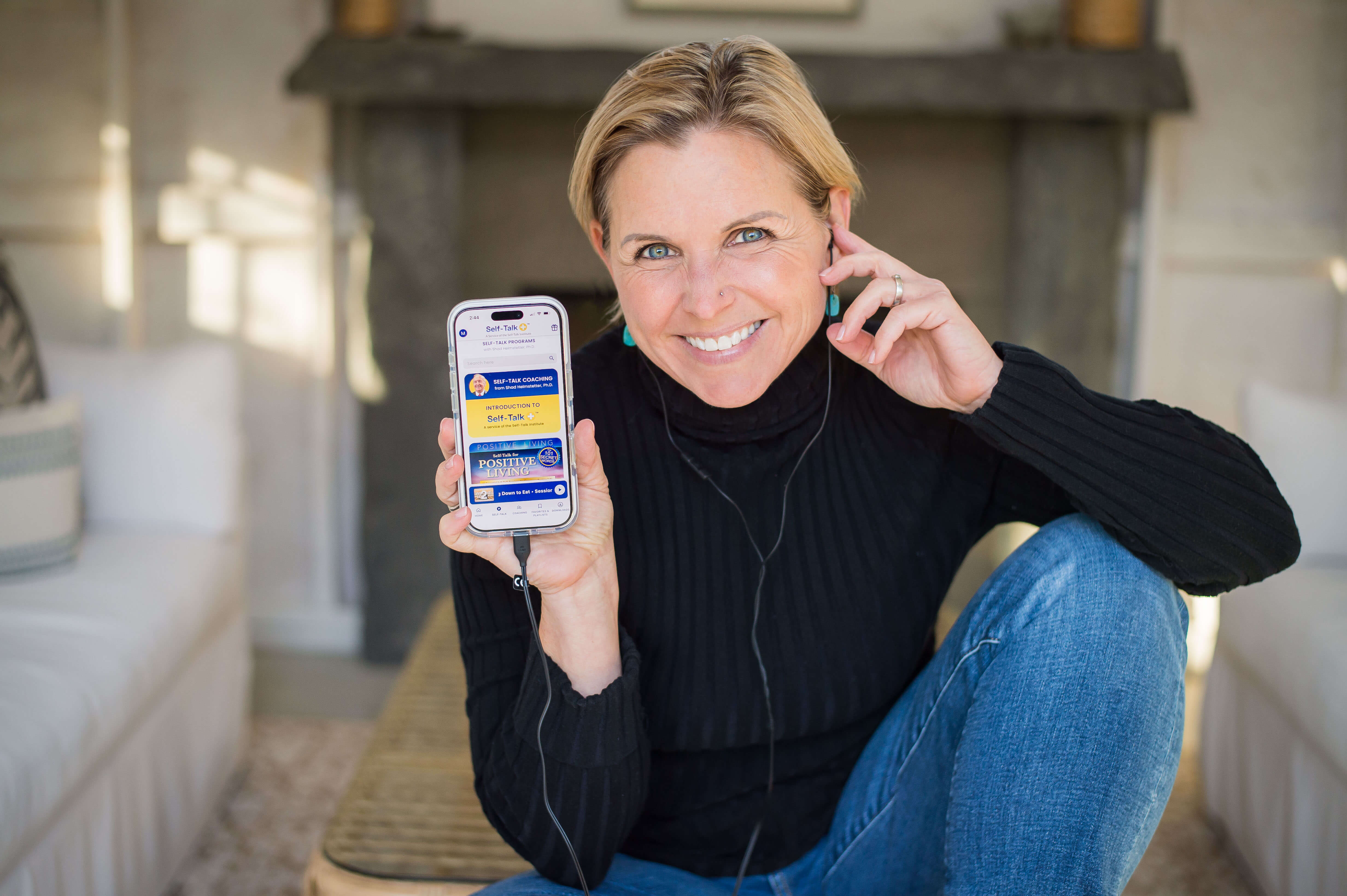Image of middle aged white woman holding up her cell phone with the Self-Talk+ app open to the first page.