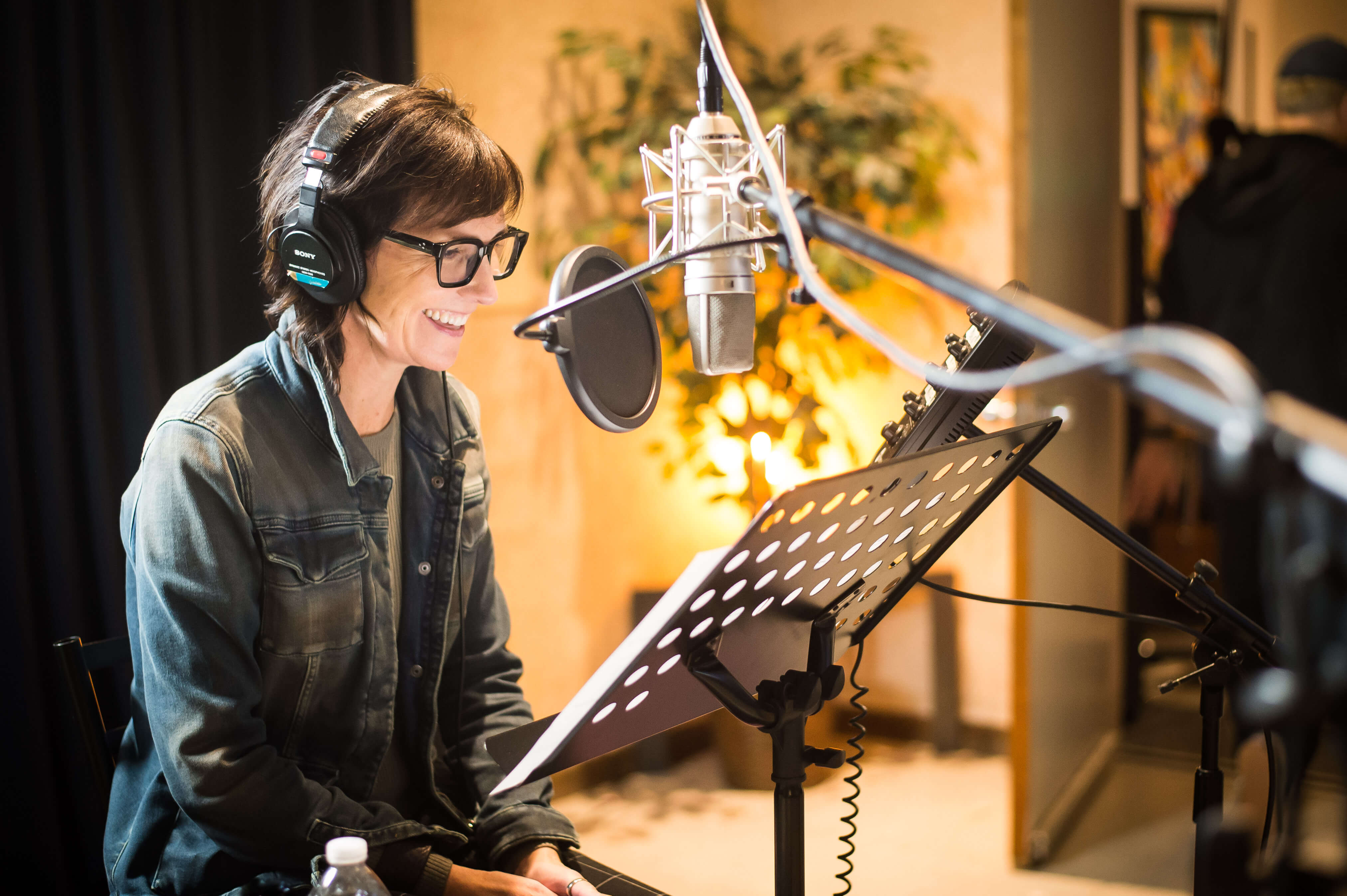 White 50-something yo woman in a sound studio with headphones on smiling at her script