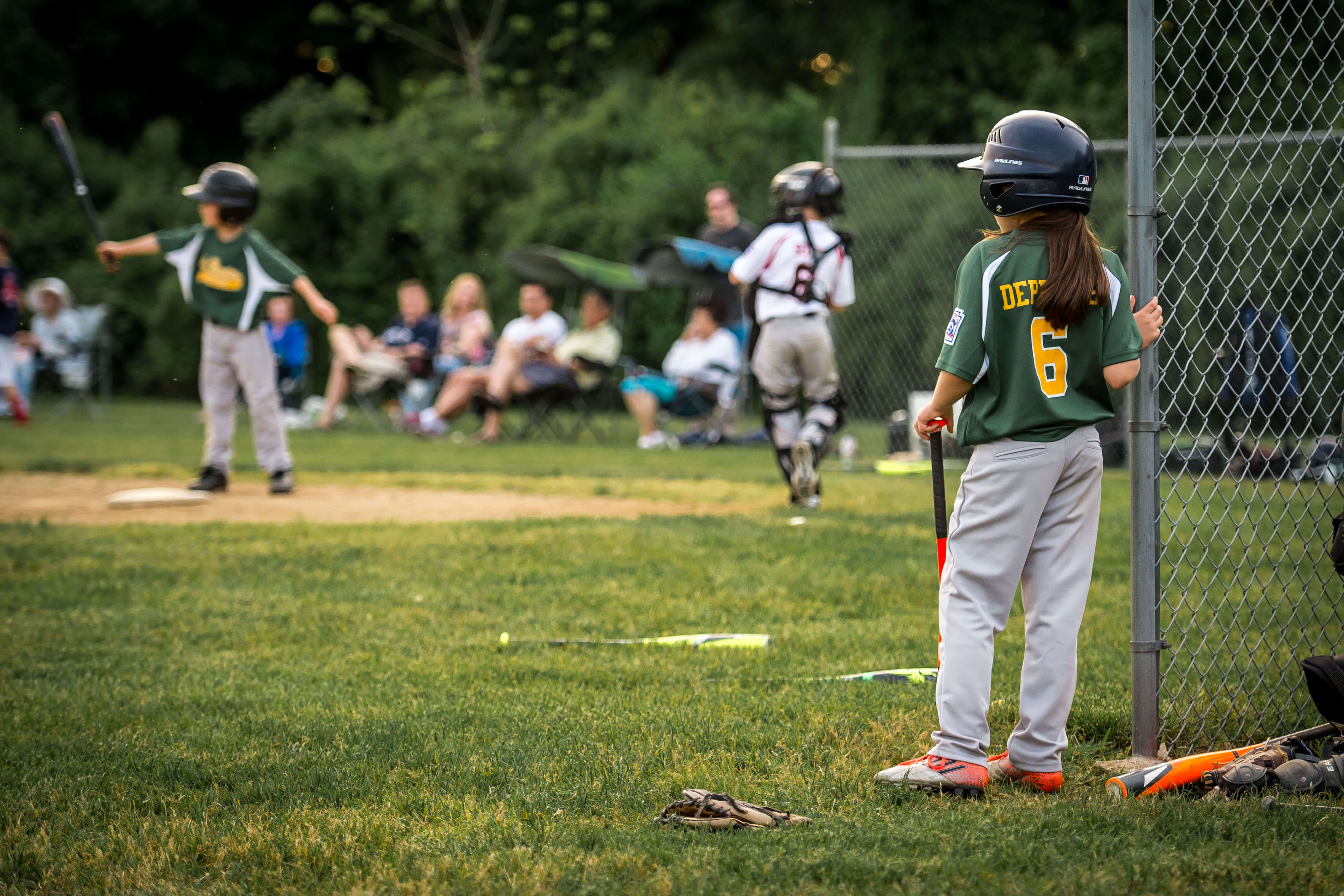 Color image of a young girl in a baseball uniform looking out at the game going on in the distance.