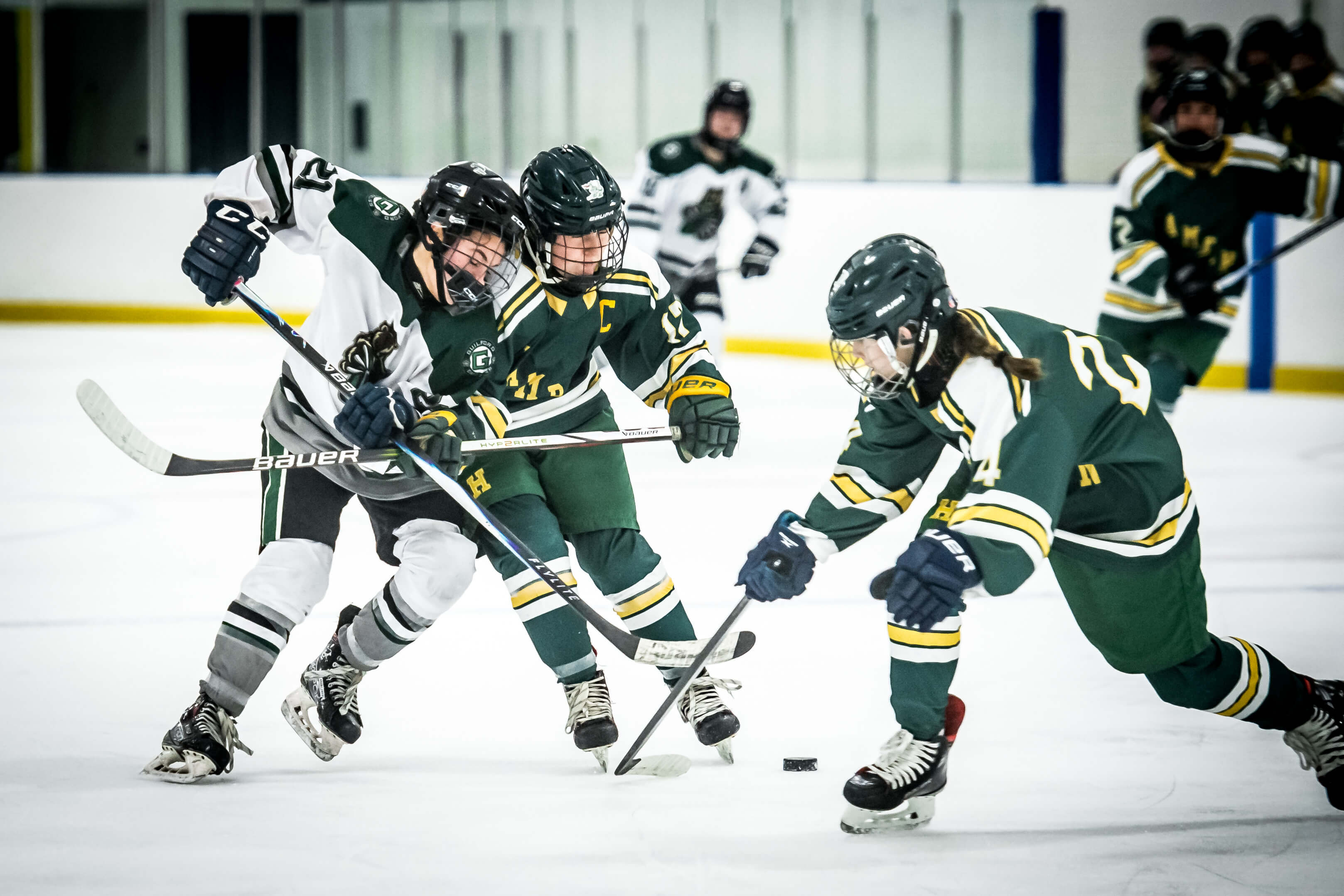 Color image of a high school girls hockey game where a player is checking another player and her helmet is coming off of her head.